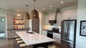 A modern kitchen with a large island, stainless steel appliances, and a bar area with stools. - Lake Alexander + Sleeps 4 Families + Lakeside + Fire Pit (Cushing)
