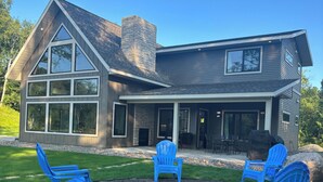 A modern two-story house with a large patio area featuring blue Adirondack chairs and a fire pit. - Lake Alexander + Sleeps 4 Families + Lakeside + Fire Pit (Cushing)
