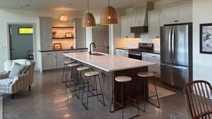 A modern kitchen with a central island, bar stools, stainless steel appliances, and pendant lighting. - Lake Alexander + Sleeps 4 Families + Lakeside + Fire Pit (Cushing)