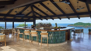 A bar area with a curved counter, multiple bar stools, and a view of the ocean. - Nekajui Peninsula Papagayo, a Ritz-Carlton Reserve Residence (Papagayo)