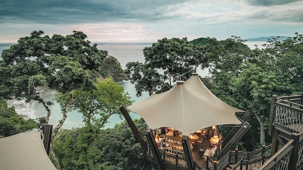 A treehouse with a wooden staircase and a canopy, overlooking a coastal landscape with dense foliage and a view of the sea. - Nekajui Peninsula Papagayo, a Ritz-Carlton Reserve Residence (Papagayo)