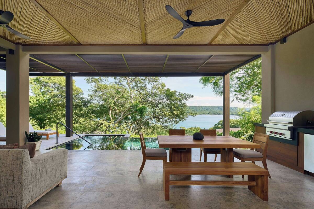 A spacious outdoor area with a wooden table and chairs, a grill, and a view of a lake.