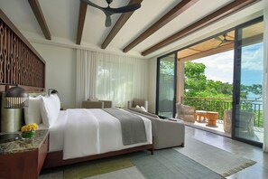 Una habitación de hotel moderna con una cama grande, un sofá, un balcón con mobiliario exterior y vistas al verdor.