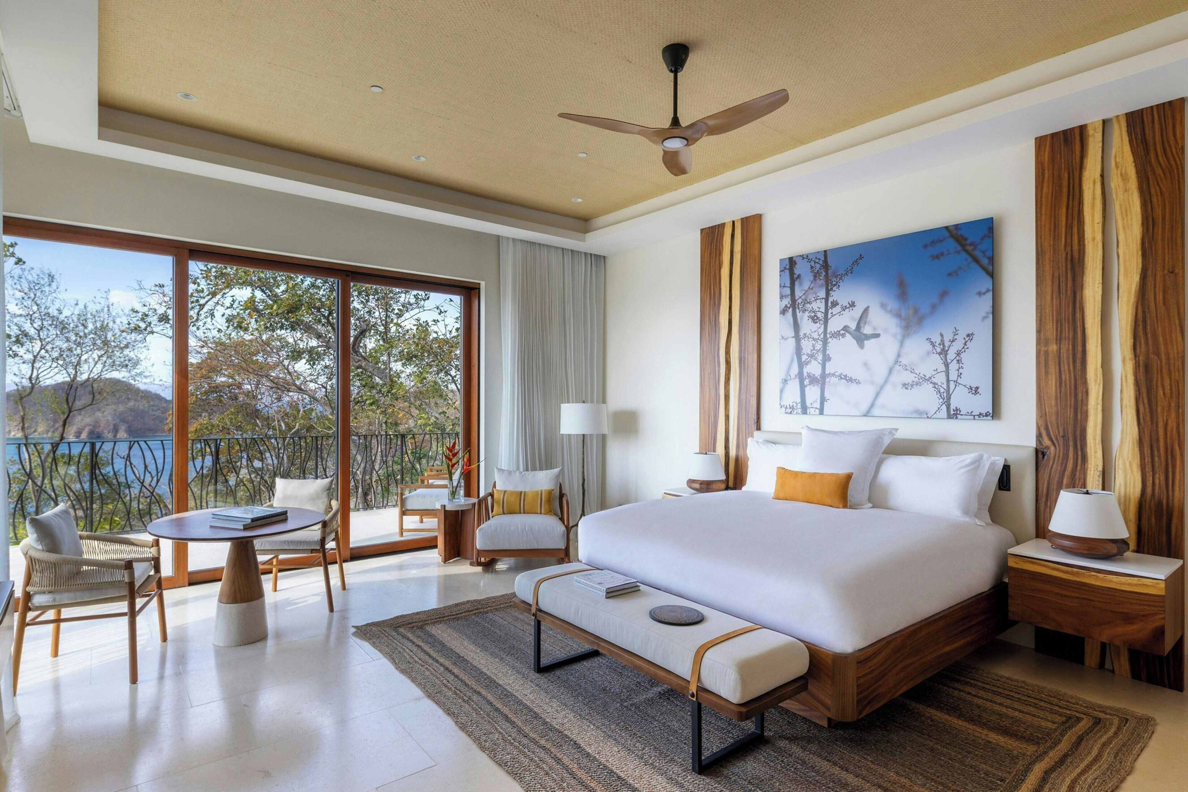 Una habitación de hotel moderna con una cama grande, una zona de comedor con sillas, una mesa y vistas al exterior.