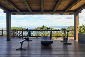 An outdoor gym with exercise equipment, a wooden deck, and a view of a body of water and hills.