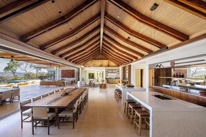 A spacious open-plan kitchen and dining area with a high wooden ceiling, large windows, and a view of the outdoors.