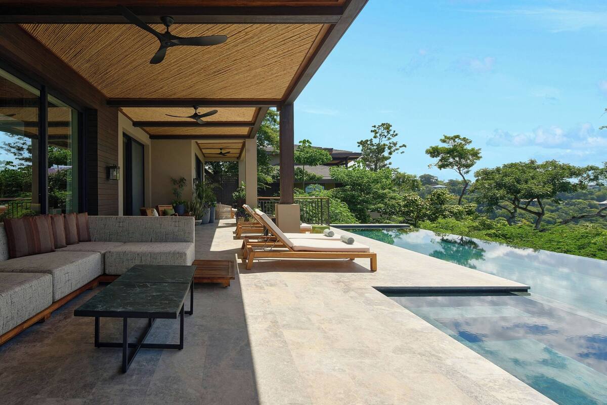 A modern outdoor lounge area with a pool, seating, and a view of the landscape.