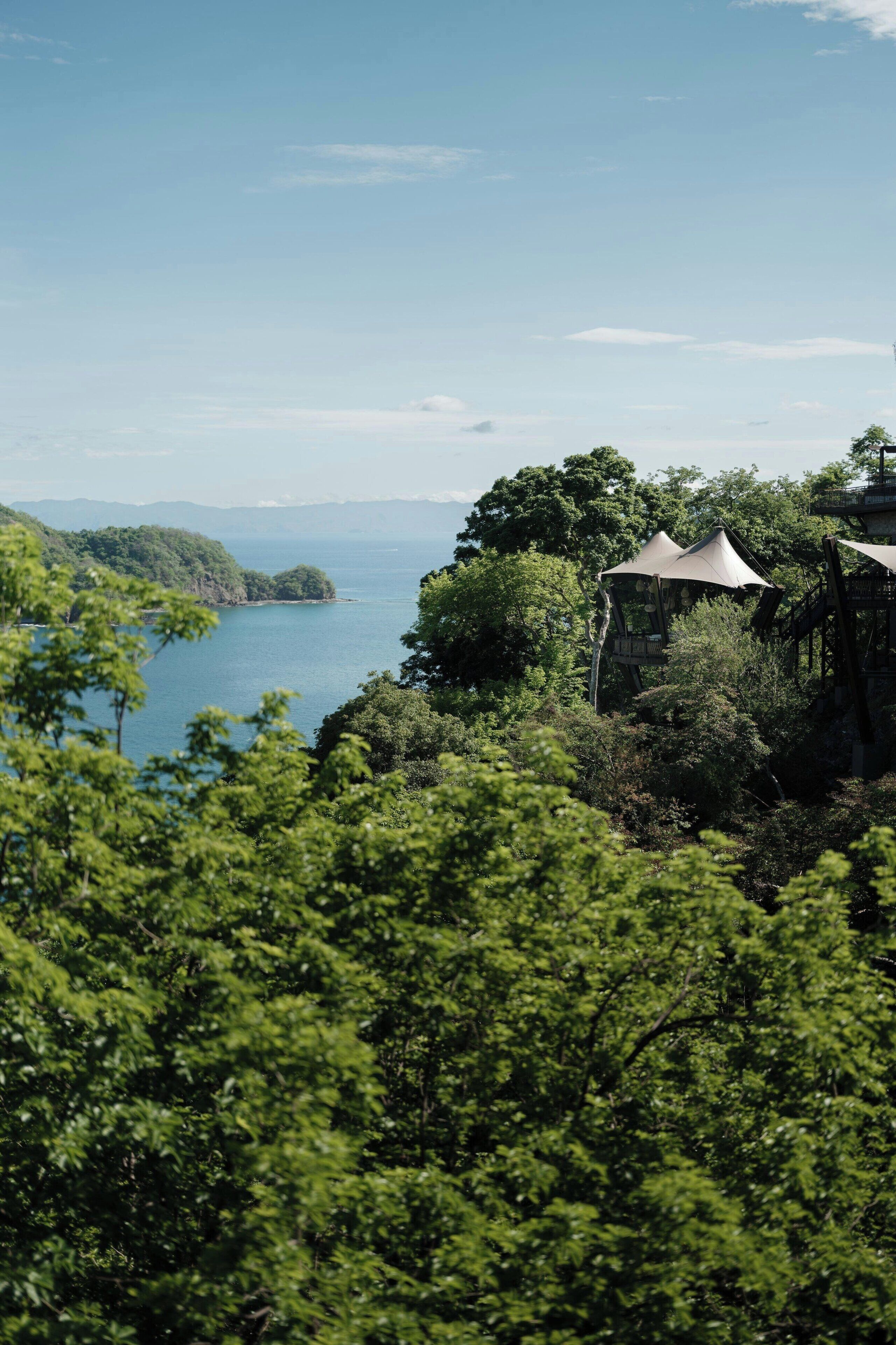 Üppige grüne Landschaft mit einem Gewässer, einem pavillonartigen Bauwerk und fernen Bergen.