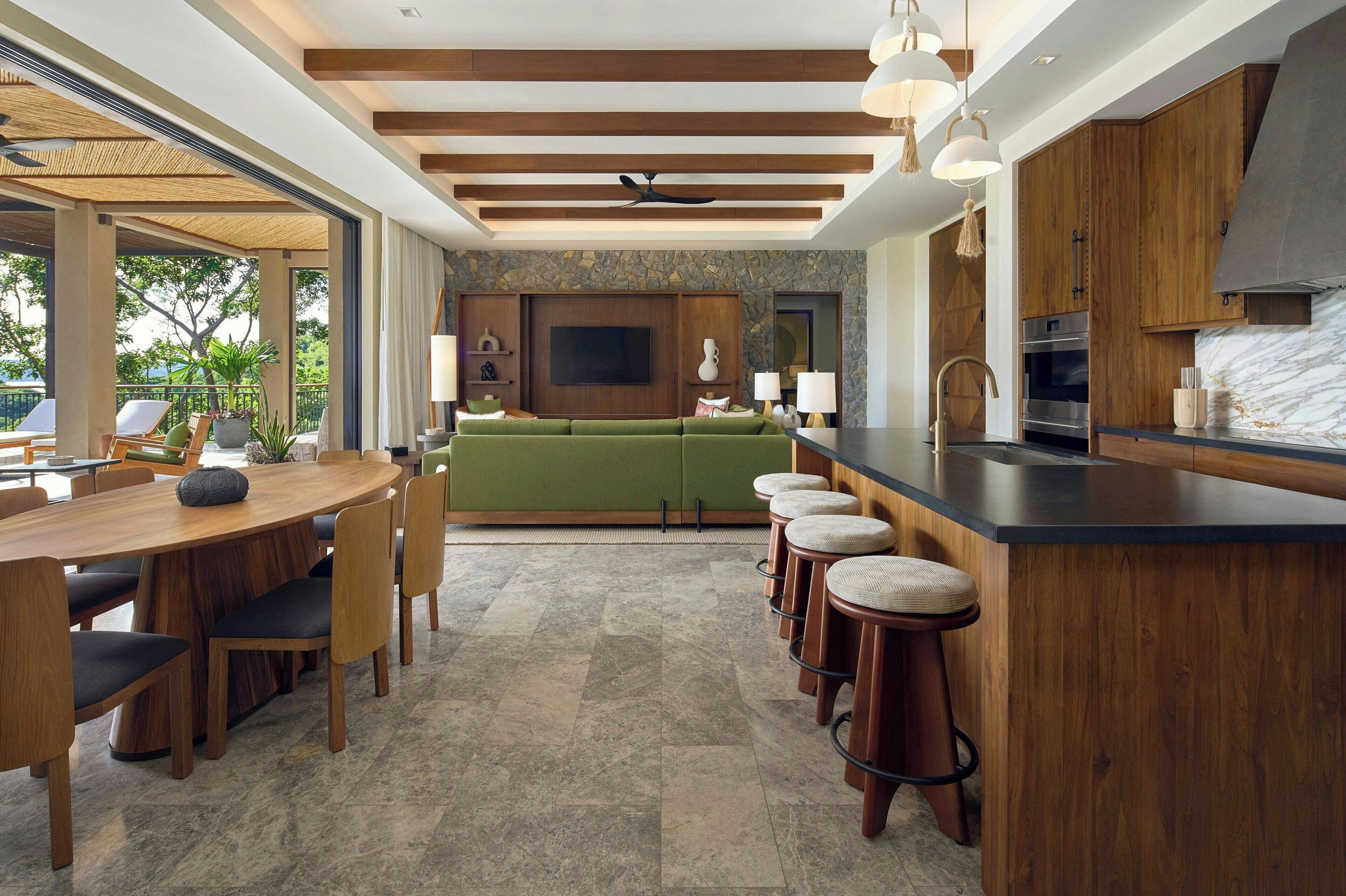 A modern kitchen with a stone backsplash, wooden cabinets, a green sofa, and a bar area with stools.