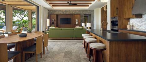 A modern kitchen with a stone backsplash, wooden cabinets, a green sofa, and a bar area with stools.