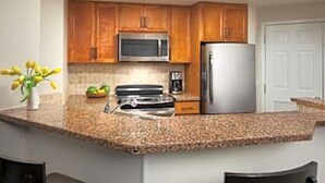 A kitchen with wooden cabinets, a stainless steel microwave, a refrigerator, and a granite countertop. - Coachell - Marriott Shadow Ridge (Palm Desert)