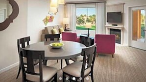 A hotel room with a round dining table, four chairs, a television, a fireplace, and a view of a golf course. - Coachell - Marriott Shadow Ridge (Palm Desert)
