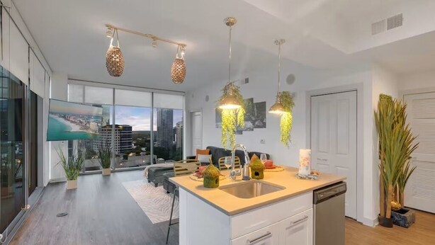 Une cuisine moderne dotée d’un îlot central, de luminaires suspendus et offrant une vue sur le paysage urbain grâce à de grandes fenêtres.