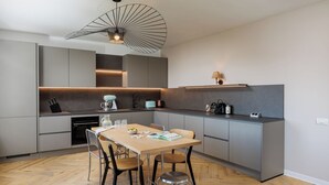 A modern kitchen with a central island, built-in appliances, and a dining area with wooden flooring and metal chairs.