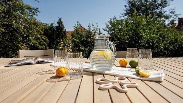 A wooden table with a pitcher of lemonade, glasses, and lemons.