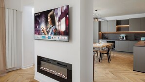 A modern kitchen with a built-in oven, a dining area with a table and chairs, and a wall-mounted flat-screen TV displaying streaming services.
