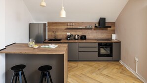 Een moderne keuken met een houten aanrecht, een inbouwoven en een zwarte vaatwasser. Er staan twee krukken bij en er hangt een hanglamp.