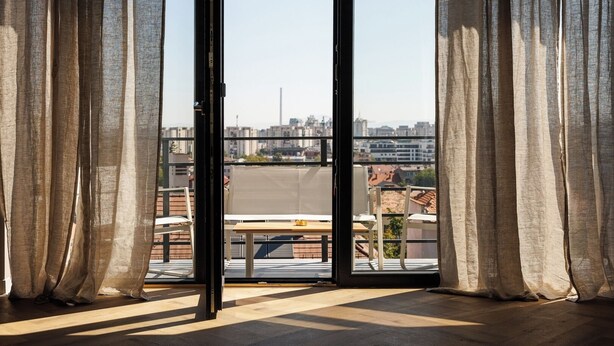 Een kamer met grote ramen van vloer tot plafond, een houten vloer en uitzicht op een stadsgezicht.