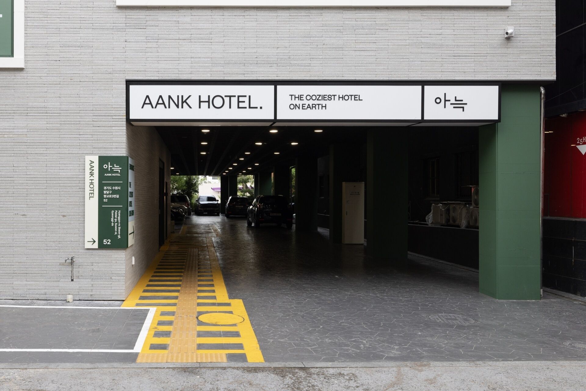 L’entrée de l’hôtel AANK, avec une enseigne au-dessus de la porte et un panneau indicateur sur la gauche.