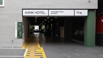 L’entrée de l’hôtel AANK, avec une enseigne au-dessus de la porte et un panneau indicateur sur la gauche.