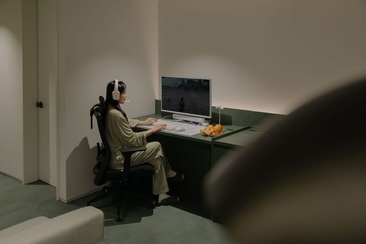 A person sitting at a desk with a computer, headphones, and a keyboard.