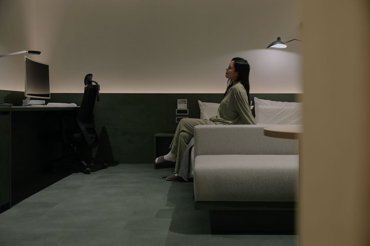 A room with a bed, a desk with a computer, and a lamp.