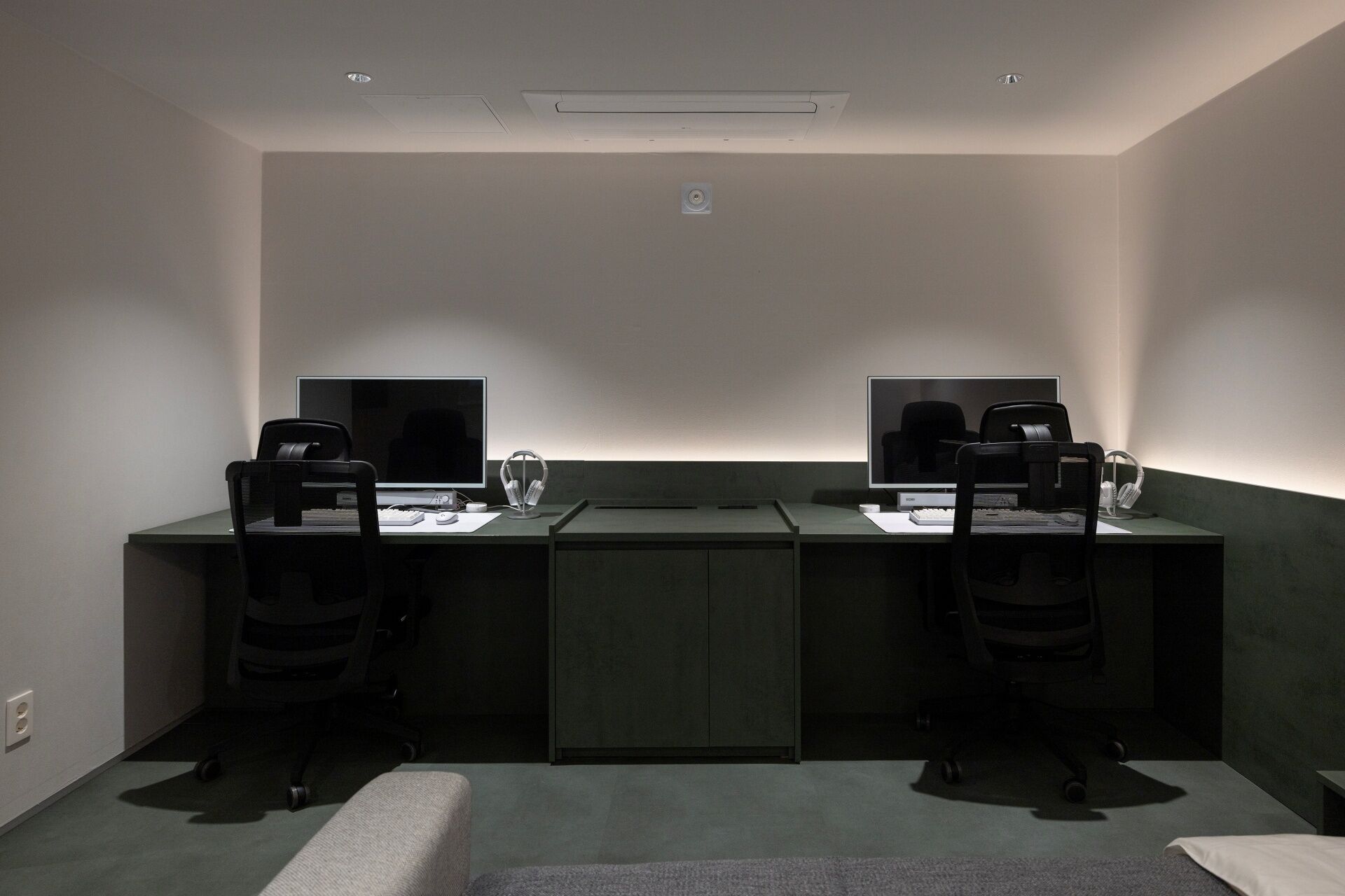 A modern, dimly lit office space with two desks, each equipped with a computer, headphones, and a coffee machine.