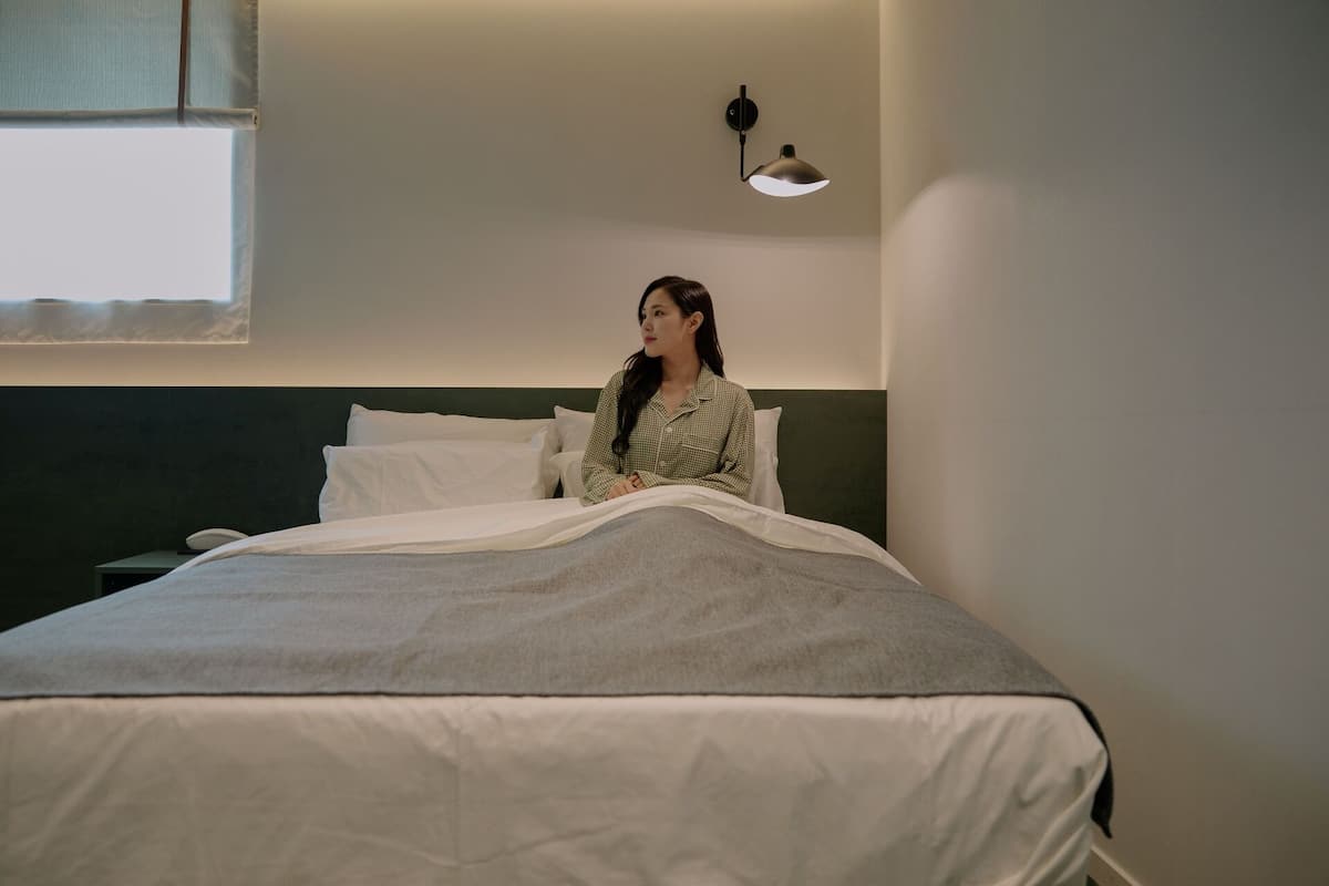 A bed with white bedding, a dark headboard, and a wall-mounted lamp.