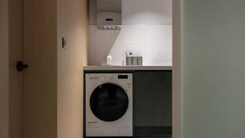 A compact kitchen with a built-in washer and dryer, a small countertop, and a tiled backsplash.