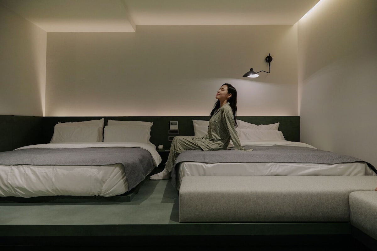 A hotel room with two single beds, a nightstand, and a wall-mounted lamp.