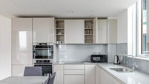 A modern kitchen with white cabinets, a built-in oven, a microwave, and a sink.