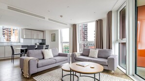 A modern living room with a grey sofa, a round coffee table, and a dining area with a kitchen in the background.