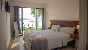 A bedroom with a large bed, two bedside tables with lamps, a view of a balcony, and a door leading to an outdoor area.
