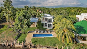 A modern house with a pool, surrounded by lush greenery and palm trees.