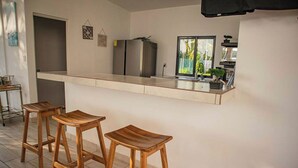 A modern kitchen with a long countertop, a refrigerator, and two wooden stools.