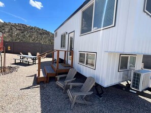 A white mobile home with a deck, outdoor seating, and a gravel driveway.