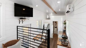 Un interior moderno con un televisor de pantalla plana montado en la pared, una escalera con barandilla metálica y una zona de cocina con fregadero y encimera.