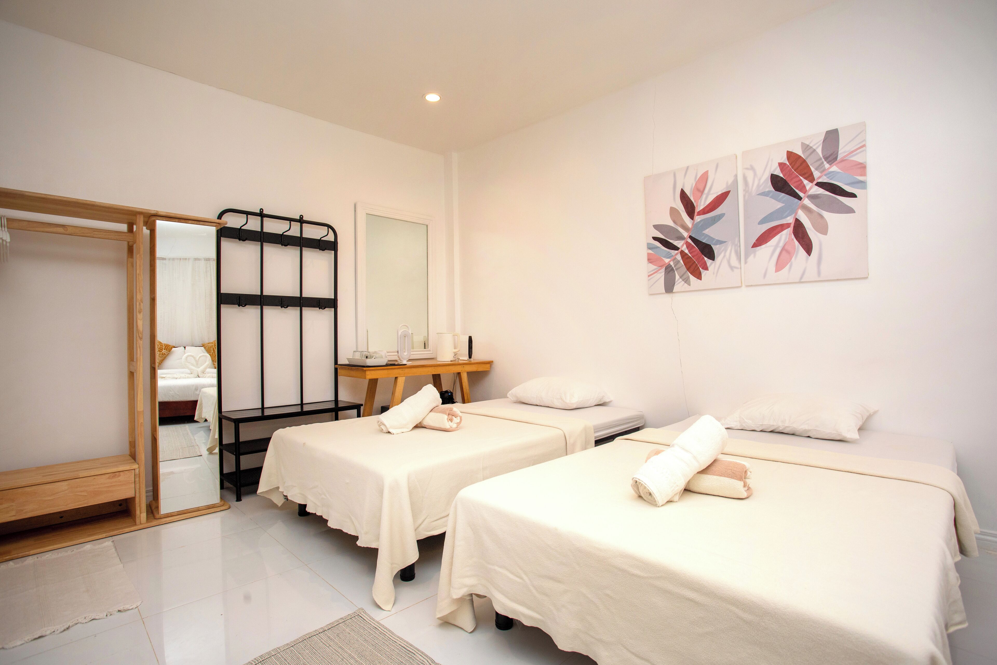 A hotel room with two beds, a wooden bench, a mirror, a small table with a lamp, and artwork on the wall.