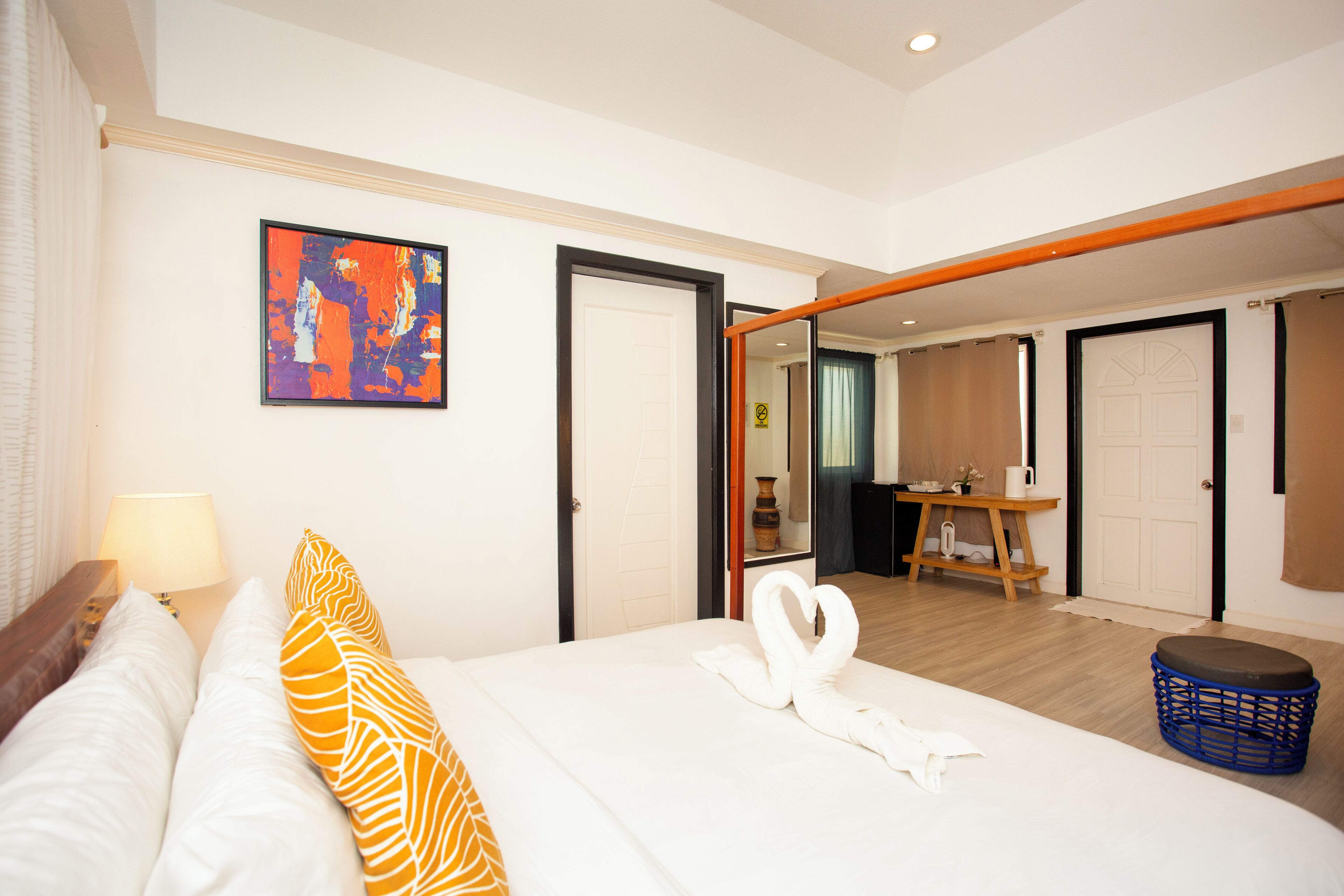 A hotel room with a bed, a nightstand, a lamp, a painting, and a bathroom visible through an open door.