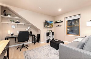 A modern living room with a desk, office chair, sofa, and a TV mounted on the wall. - Charming 1-bedroom Guest suite in beautiful Black Forest. (Colorado Springs)