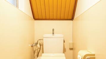 A small, compact bathroom with a wooden ceiling, a toilet, a hand dryer, and a window.