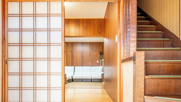 Un intérieur de style japonais traditionnel, avec un escalier en bois, des portes coulissantes et un canapé à l’arrière-plan.