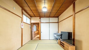 Une pièce de style japonais traditionnel, avec un sol recouvert de tatamis, une porte coulissante, un téléviseur et une petite table.