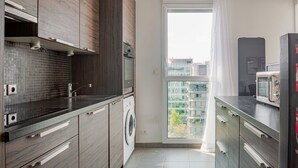 Eine moderne Küche mit Waschmaschine, Mikrowelle und Blick auf eine Stadtlandschaft durch ein großes Fenster.