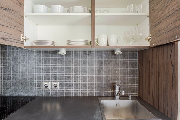 A kitchen with a black countertop, a stainless steel sink, and a tiled backsplash.