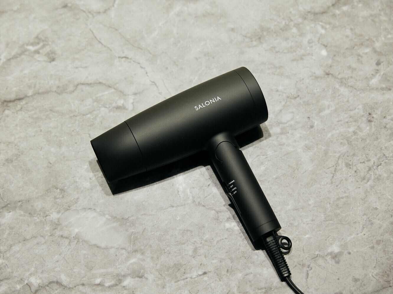 A black hair dryer with a cord on a textured surface.