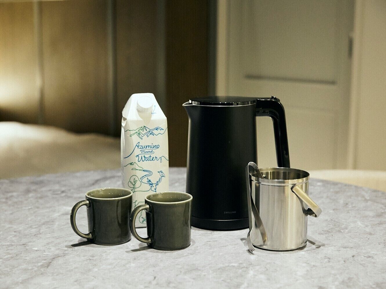 Eine Küchenarbeitsplatte mit einer Milchpackung, einer schwarzen Kaffeekanne und zwei Edelstahlbechern.