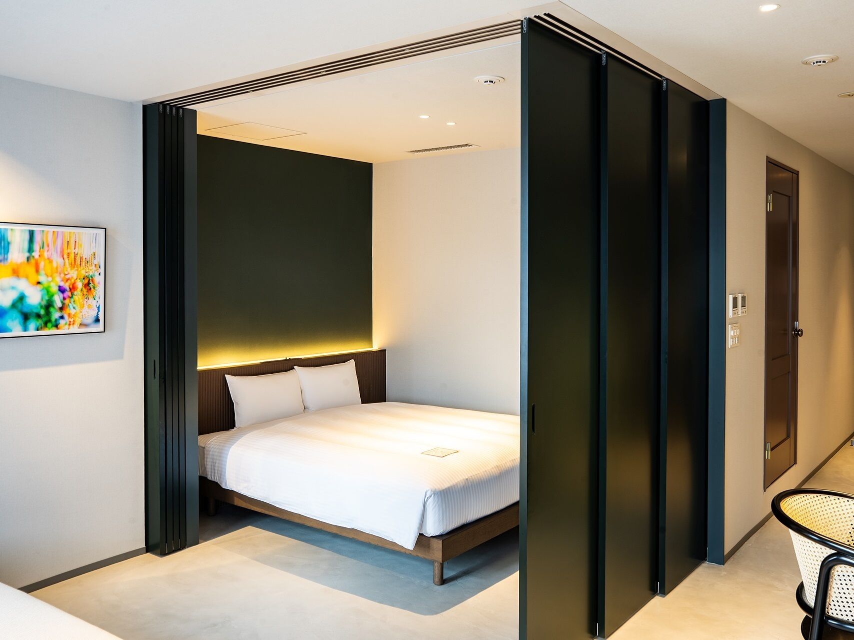 Um quarto moderno com cama, uma obra de arte na parede e uma porta que dá para outro cômodo.