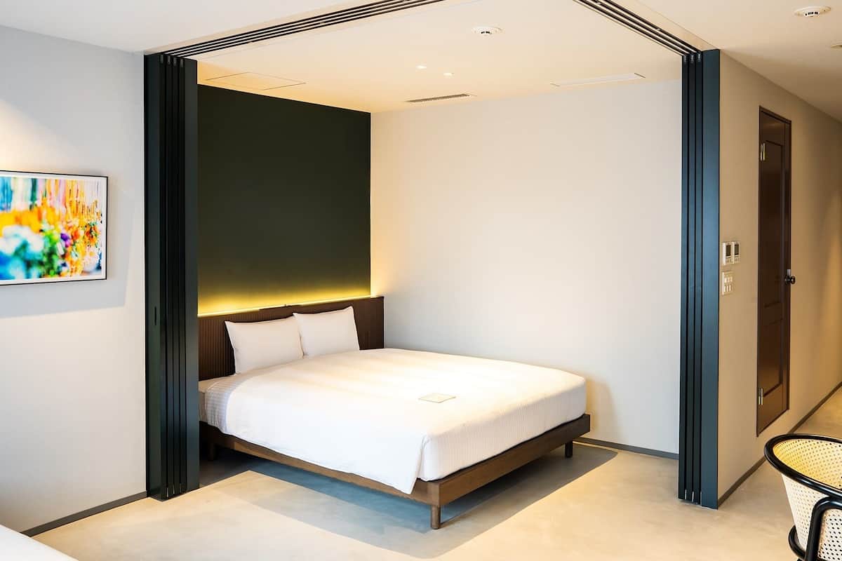 A modern bedroom with a bed centered in a room with a dark accent wall, a visible door, and a chair.