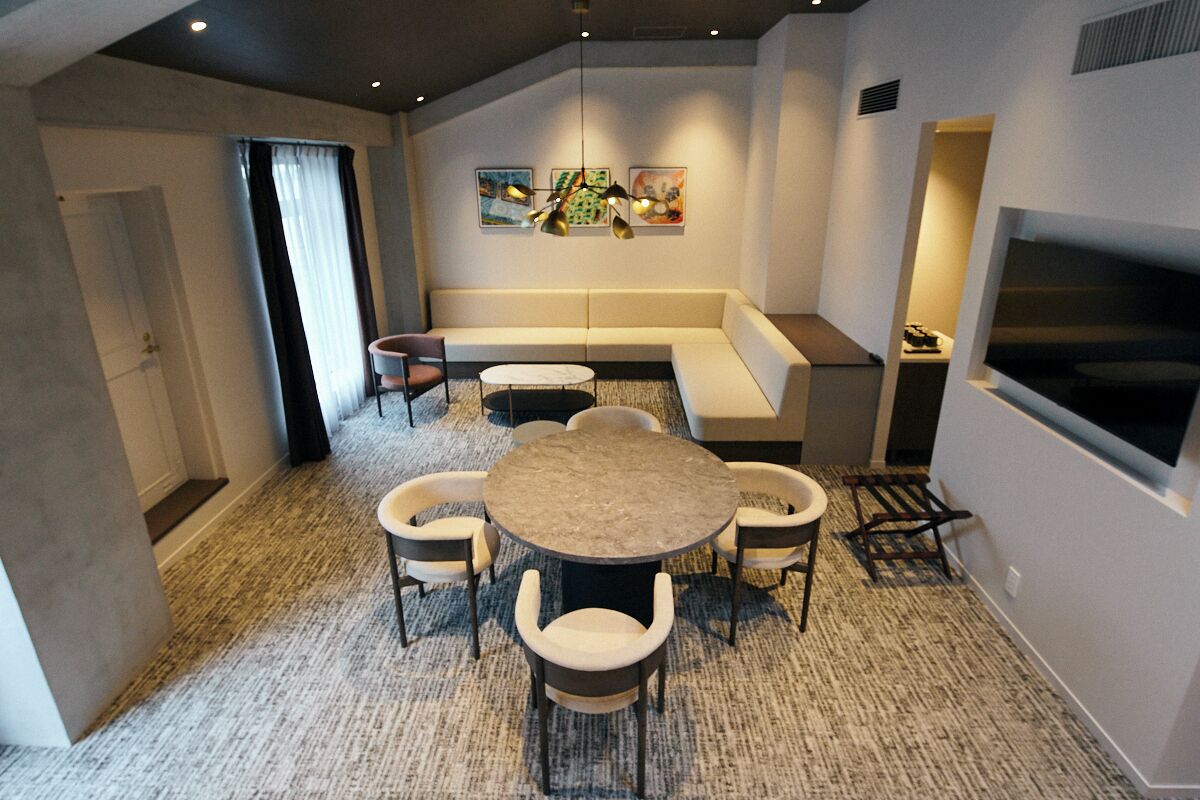 Una habitación de hotel moderna con una mesa redonda, cuatro sillas, un sofá y un televisor.